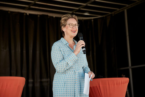 A person in a blue dress speaks radiantly into a microphone.