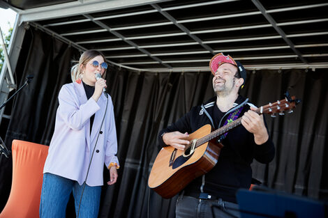 Two people on a stage, left with microphone, right with guitar.