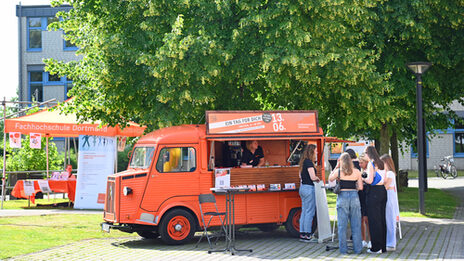 People stand in front of the orange-colored HY of Fachhochschule Dortmund.