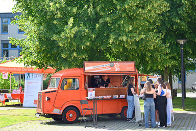 People stand in front of the orange-colored HY of Fachhochschule Dortmund.