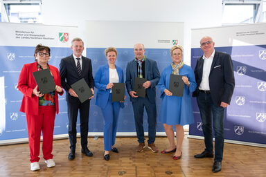 Six people stand next to each other, five of them holding a folder in front of them.