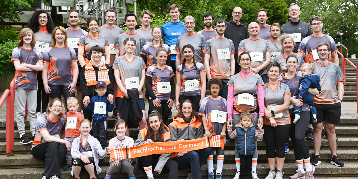 Rund 40 Menschen in Sportkleidung stehen und sitzen auf einer Treppe vor Büschen im Hintergrund.