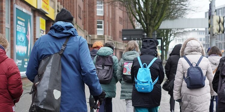 Mehrere Personen mit dicken Jacken und Rücksäcken spazieren durch die Stadt.