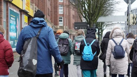 Several people with thick jackets and backpacks walk through the city.