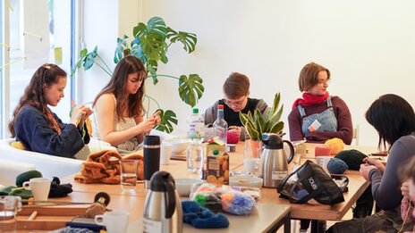Several concentrated knitters sit at a table generously laid with juices and cookies