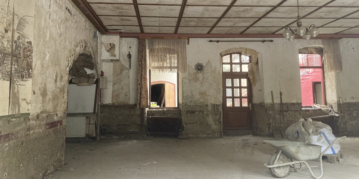 There is a wheelbarrow in an empty apartment, the dirty walls and broken windows make the room look like a building site.