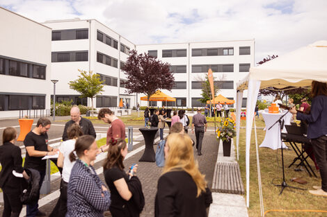 Impression of the Summer Festival 2022. People stand at bar tables on the Emil-Figge-Straße campus and chat while a live band plays.