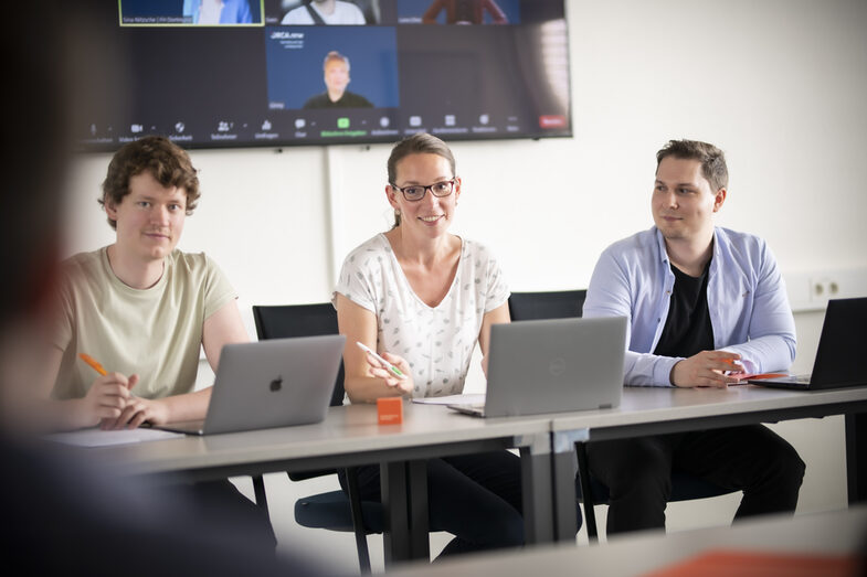 3 Mitarbeiter*innen nehmen an einer Hybriden Konferenz teil