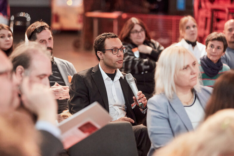 Lecturer in the audience asks a question to participants in a panel discussion.