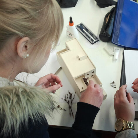 You look over the shoulder of a young woman who is working on a cardboard model of a floor