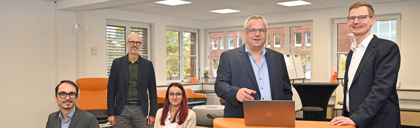 A group of people stand and sit at and around an orange desk in the User Innovation Center.
