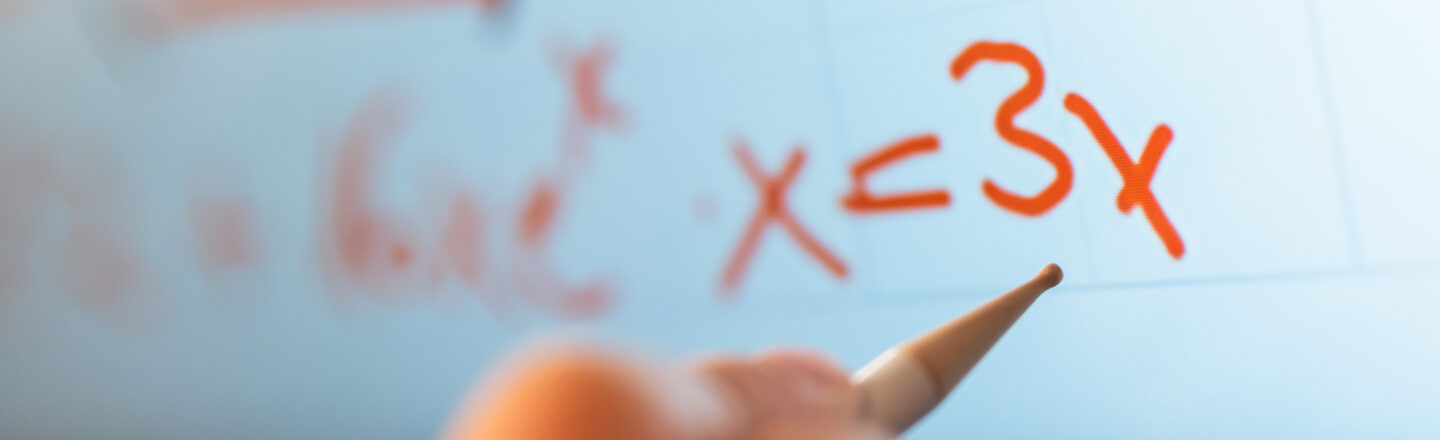 Photo of a hand with a pen for a digital board. The hand is to the board for the formula x = 3x