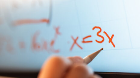 Foto von einer Hand mit einem Stift für ei digitales Board. Die Hand ist zum Board zur Formel x = 3x
