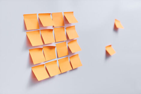 Photo of twelve orange Post-ist stuck to a wall in a square shape.