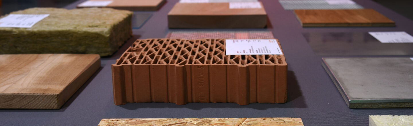 Auf einem Tisch liegen quadratische Muster unterschiedlicher Materialien aus Holz oder Stein. Sie sind versehen mit kleinen Erkläungsschildern.