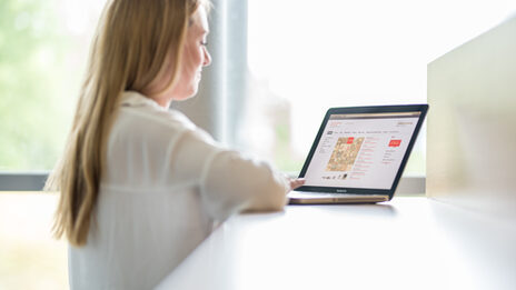 Foto einer Studentin von der Seite, die an einem Laptop arbeitet.__Young woman looks into the laptop.