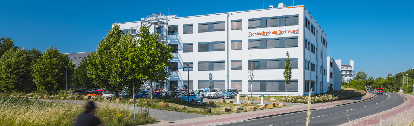 Building photo with "Fachhochschule Dortmund" logo on building 38b - from a distance. Cyclist enters the picture on the left.