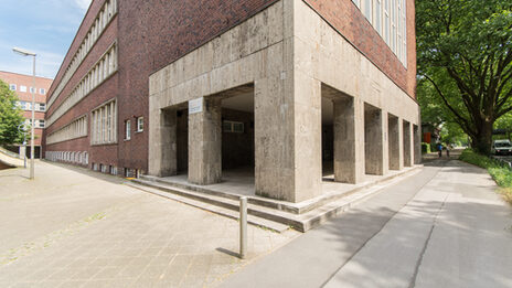 Foto mit Blick auf die Ecke eines Gebäudes der Fachhochschule Dortmund am Max-Ophüls-Platz mit Vorplatz und Gehweg.