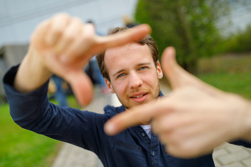 Photo of a student forming a square with his index fingers and thumb in front of him and looking through it.