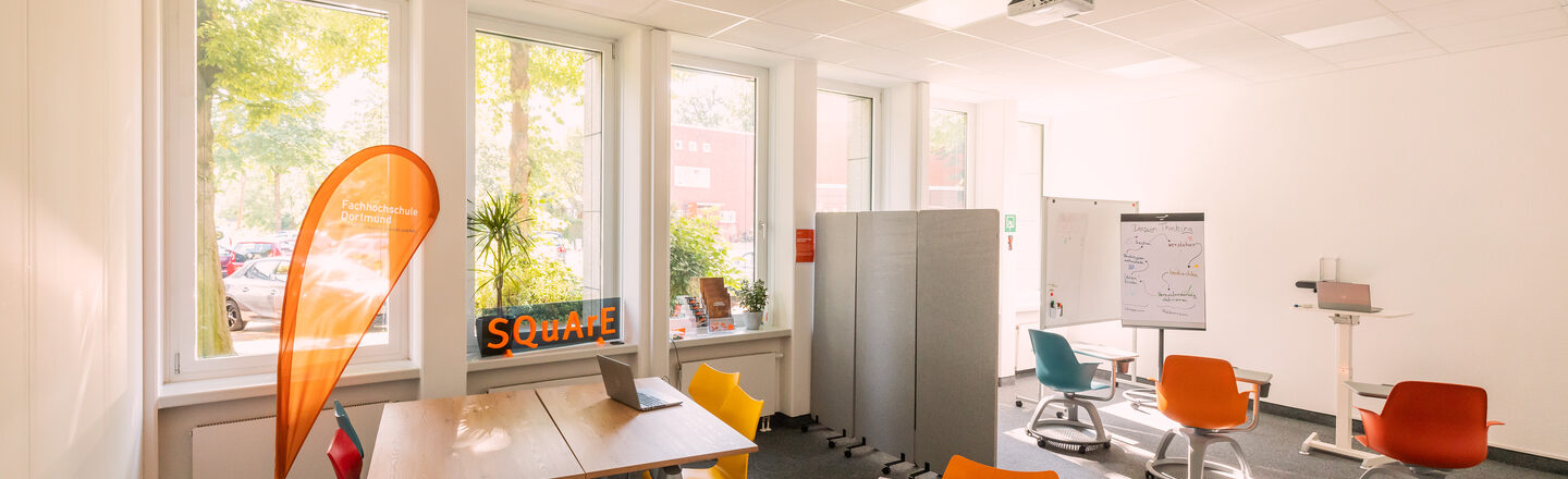 Photograph of a meeting room divided into different levels. There are two groups of tables at the front and movable chairs and mobile walls at the back.