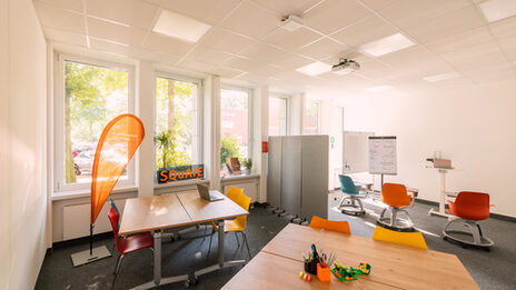 Photograph of a meeting room divided into different levels. There are two groups of tables at the front and movable chairs and mobile walls at the back.