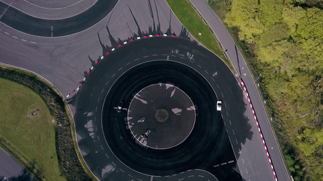 Bird's eye view of a circular track with irrigation. Test vehicles (Volvo, Spyder) are driving on it.