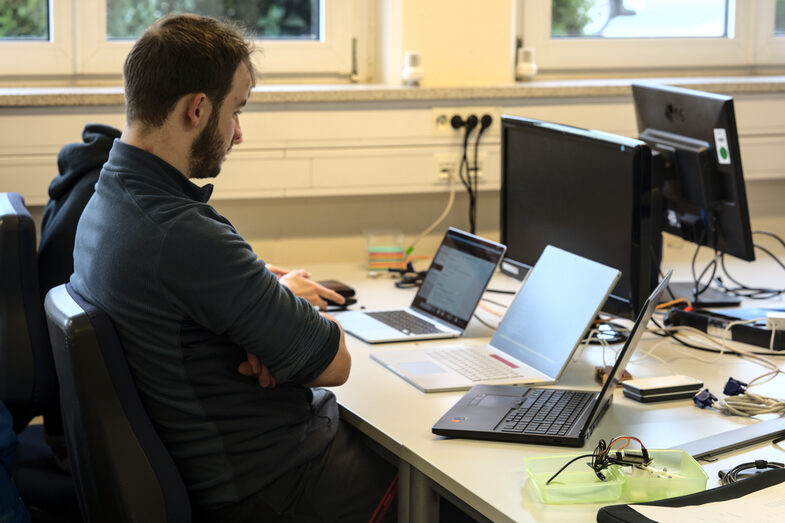 Zwei Blockwochenteilnehmer sitzen zusammen vor einem Notebook an einem Tisch und besprechen die Schnittstelle zum Greifer. Der Greifer liegt neben dem Notebook in einer Butterbrotdose auf dem Tisch.