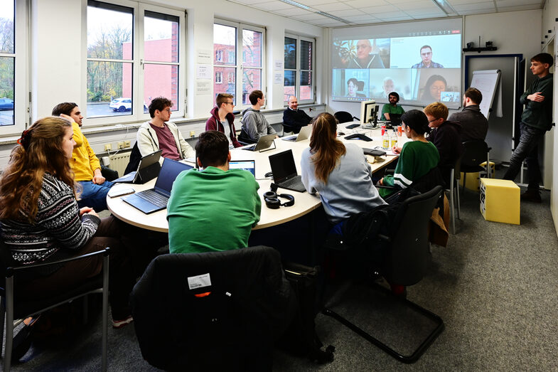 Students sit around the large table in the IDiAL meeting room and discuss the schedule for the last day of the block week with the professors connected via video conference.