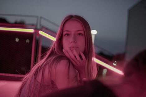 A person in red light looks just past the camera, seemingly lost in thought.