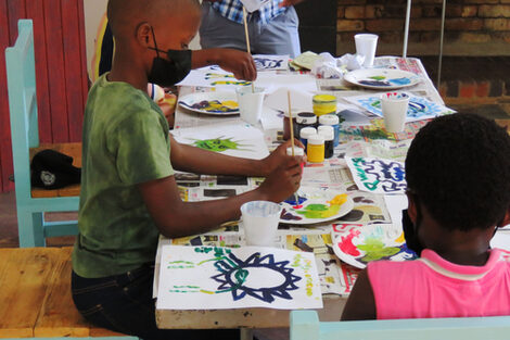 Kinder sitzen an einem Tisch und malen Bilder.