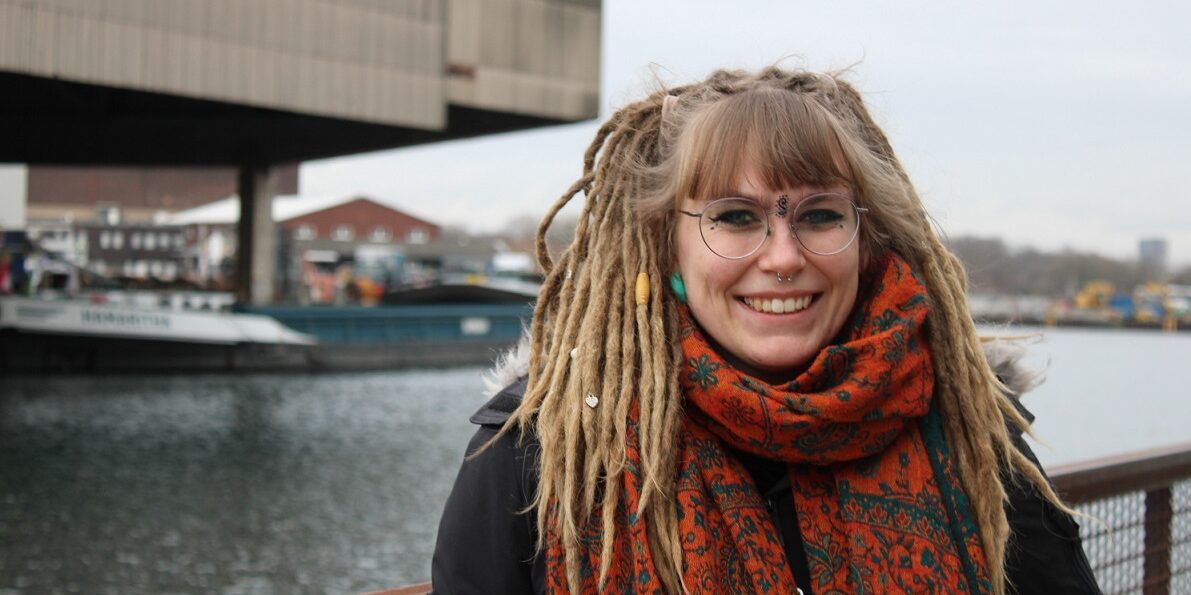 Sabrina Günther smiles into the camera. In the blurred background, a barge sails across the Dortmund-Ems Canal.