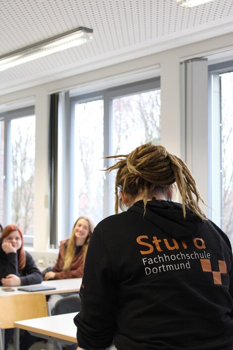 The photo is taken over the shoulder of a StudyScout. Two students are sitting at a table in the blurred background.