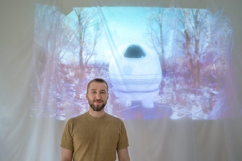 Lennart Gruensel steht lächelnd neben der Projektion von Argos, einer Künstlichen Intelligenz.