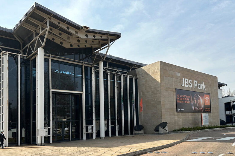 Ein Gebäude mit hoher, verglaster Fassade, daneben ein Beton-Anbau mit einem großen Werbeplakat der University of Johannesburg.