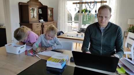 Der Stipendiat Jens Terbrack sitzt am Tisch und arbeitet an seinem Laptop. Daneben malen seine beiden Töchter Bilder.