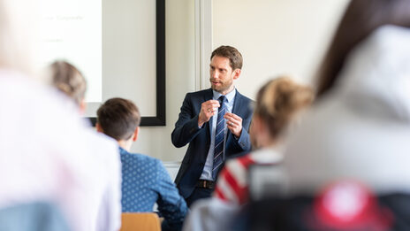 Photo of a teacher standing in front of his students and explaining something