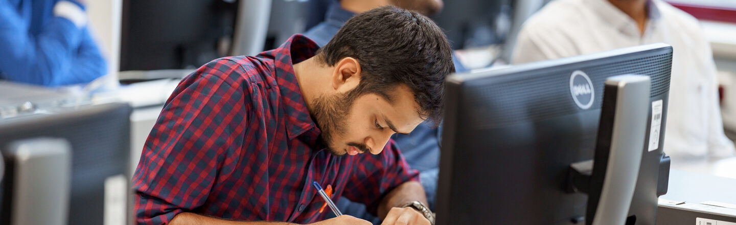 Photo of a student writing something in a notebook in the computer room.