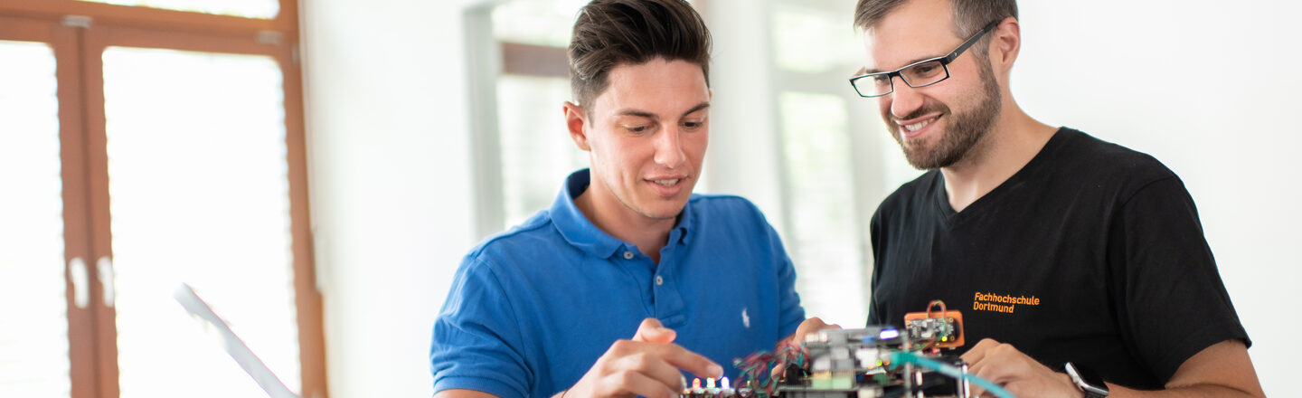 Foto eines Studenten und eines Mitarbeiters des Labors für Energieautomation und Netzführung. Sie  stehen nebeneinander und arbeiten an einem elektronischen Versuchsaufbau.