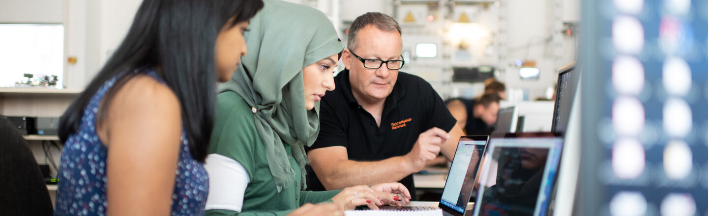 Foto von zwei Studentinnen und einem Professor im Labor für Energieautomation und Netzführung. Sie sitzen nebeneinander und schauen gemeinsam auf den Bildschirm eines Laptops.