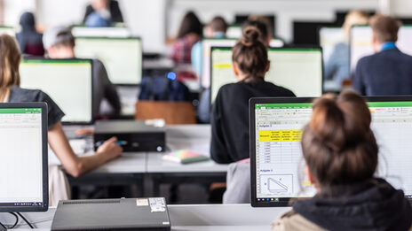 Blick von hinten in den Computerraum mit Studierenden, auf den Monitoren sind zum Teil Excel-Tabellen erkennbar.