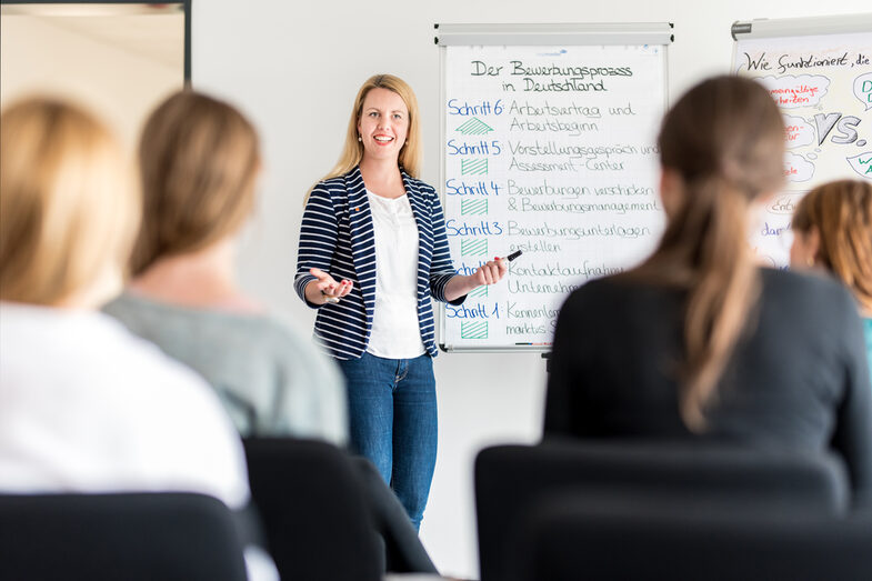 Photo of a member of staff from the Career Service standing in front of a flipchart outlining the application process in Germany. Several students are sitting in front of her, listening to her.