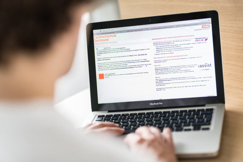 Photo over the shoulder of a man looking into a laptop. On the screen you can see the Fachhochschule Dortmund's study place portal.