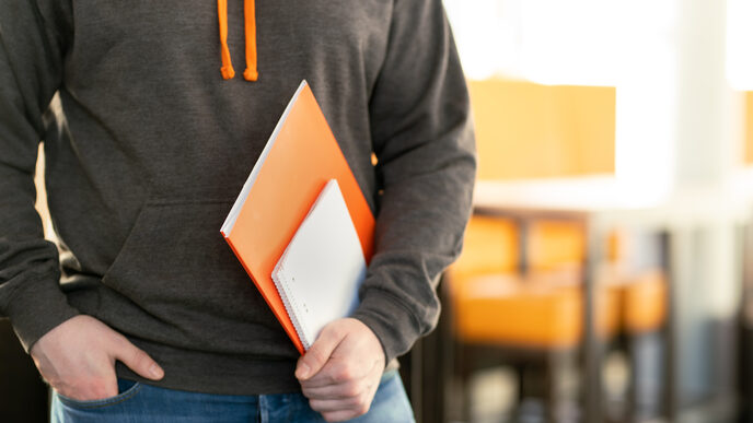 Foto eines Studenten - kopfabwärts - der einen Pullover mit dem Logo der Fachhochschule Dortmund trägt und einige Mappen und Blöcke in seiner Hand hält. __ A student wears a sweater with the logo of the Dortmund University of Applied Sciences and holds some folders and pads in his hand.