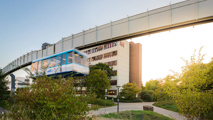 Foto der H-Bahn-Schienen mit vorbeifahrender H-Bahn, im Hintergrund des Gebäude Emil-Figge-Straße 44 der Fachhochschule Dortmund.