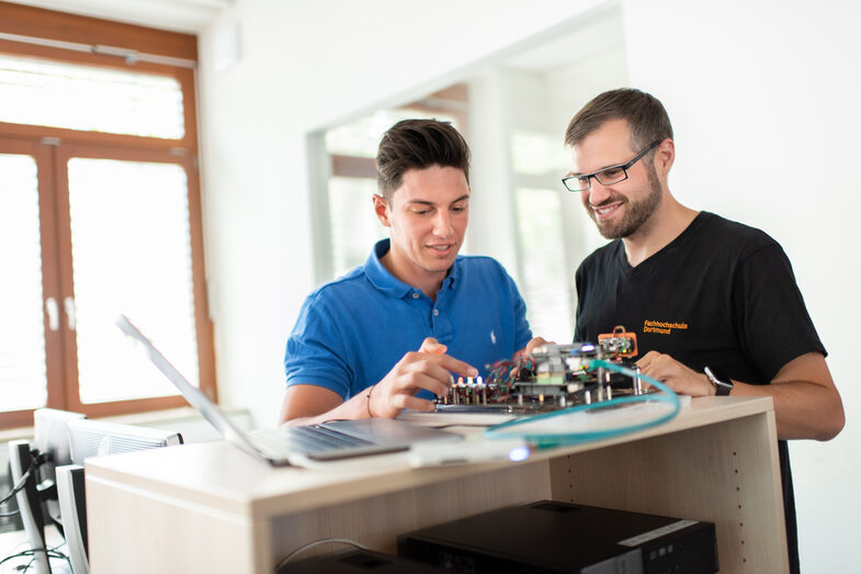 Foto eines Studenten und eines Mitarbeiters des Labors für Energieautomation und Netzführung. Sie  stehen nebeneinander und arbeiten an einem elektronischen Versuchsaufbau.