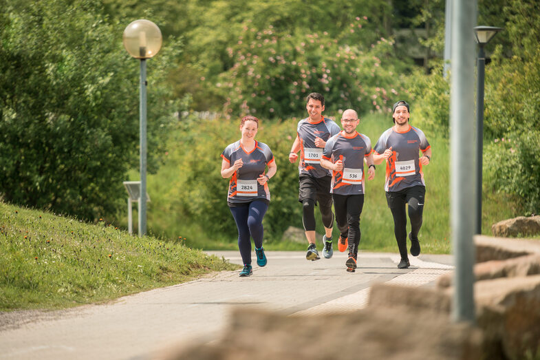 Foto von vier Mitarbeiter*innen in FH-Laufkleidung, die bei einem organisierten Lauf auf dem Campus mitlaufen.