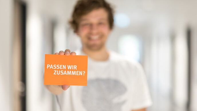 Photo of a man holding a card with the words "Do we fit together?" into the camera __Man out of focus holding a card with the words "Do we fit together?" into the camera.