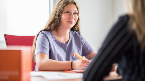 Foto einer Schülerin, die einer weiteren Frau gegenüber sitzt, welche rechts im Bild nur im Anschnitt zu erkennen ist. Sie führen ein Beratungsgespräch zur Studienberatung.