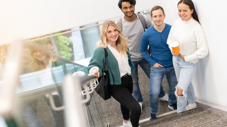 Photo of 4 students standing in a stairwell and looking up at the camera.