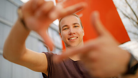 Photo of a student forming a square with his index fingers and thumb in front of him and looking through it.